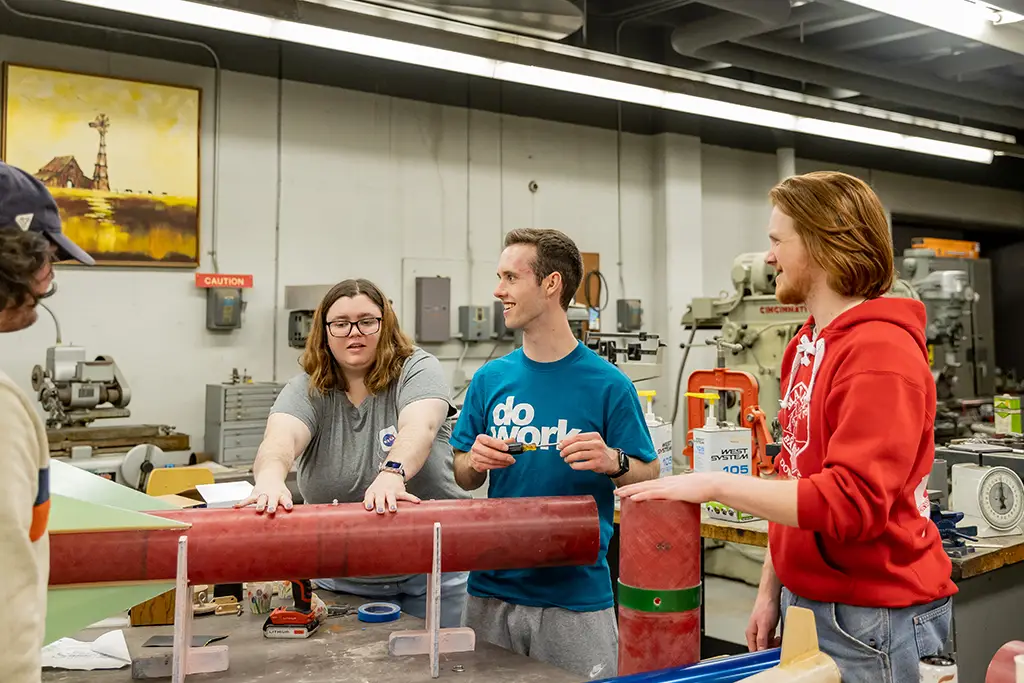 Undergraduate engineering students discussing technical assembly details while constructing a large-scale prototype in the student workshop.