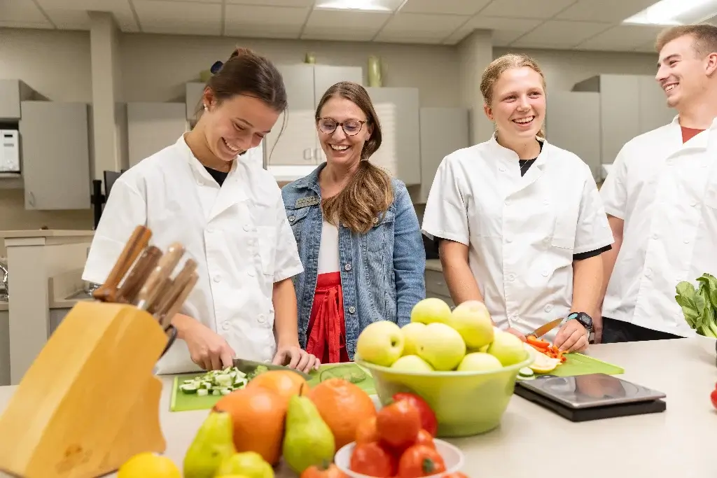 Kitchen scene with four students, nutrition majors, preparing fruit bowl for class project.