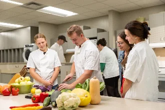 Students in a kitchen learning about food science and nutrition while preparing a meal.