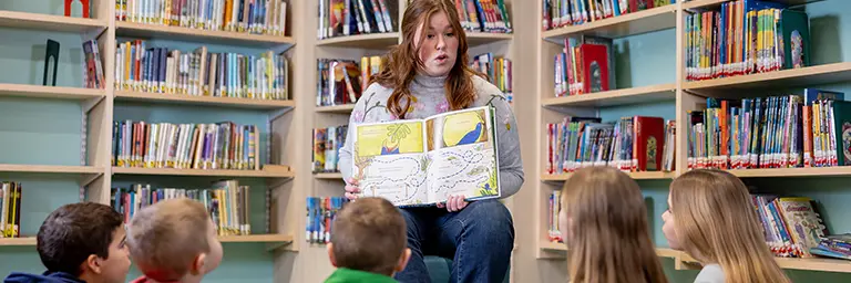 A student pursuing an early childhood education degree reading a storybook to a group of young children.