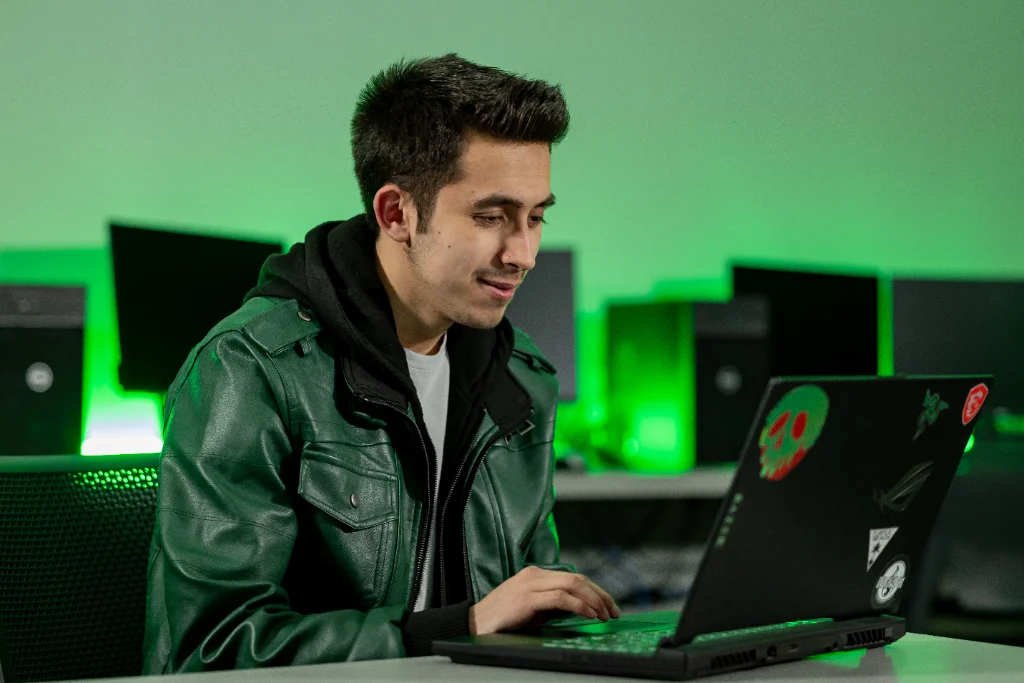 A software engineering student sitting in a computer lab, focused on coding on his laptop