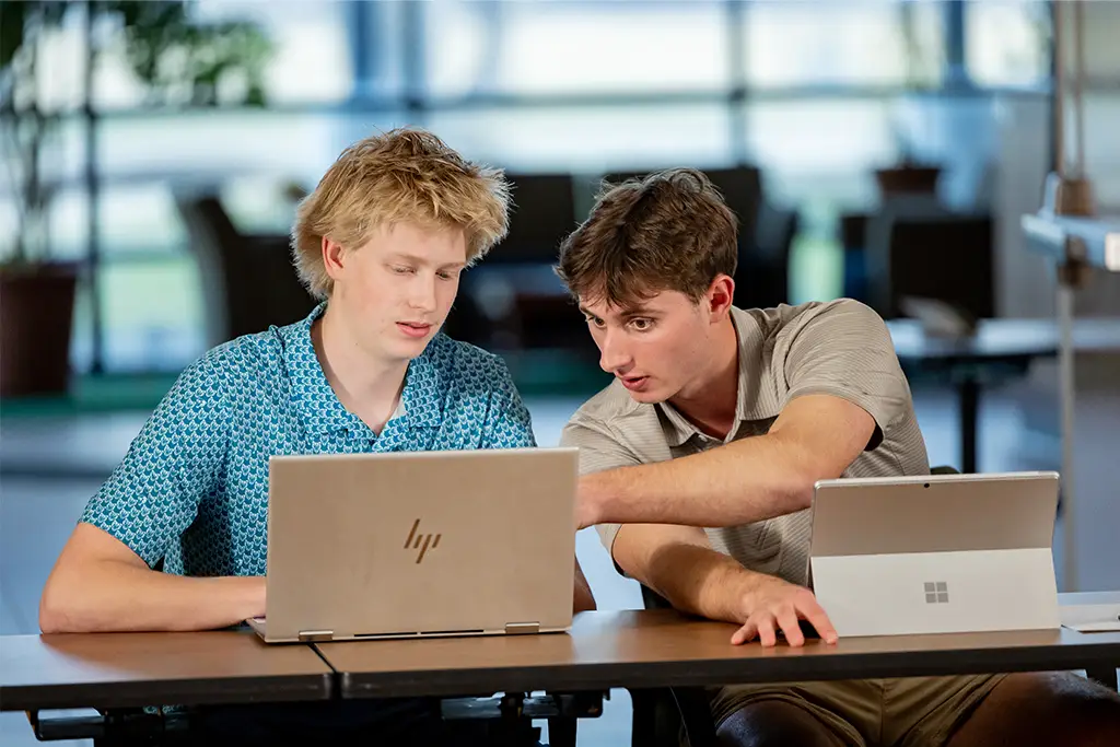 Two students collaborating on a laptop, discussing data and predictive analytics.