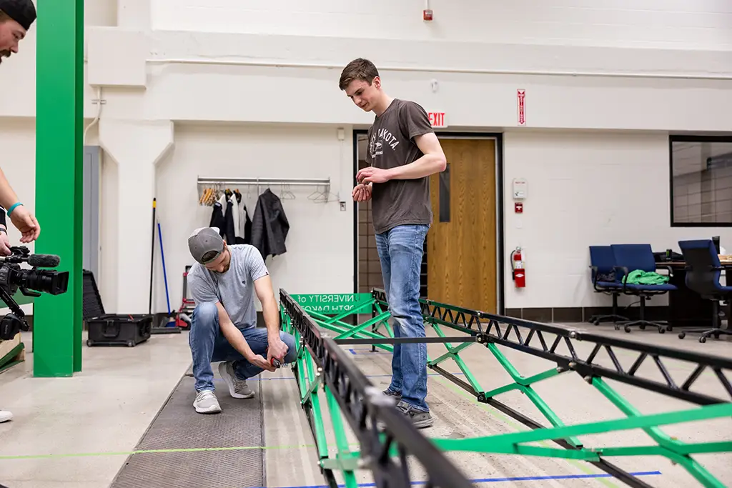 Two civil engineering students assembling a steel truss structure in the engineering lab.