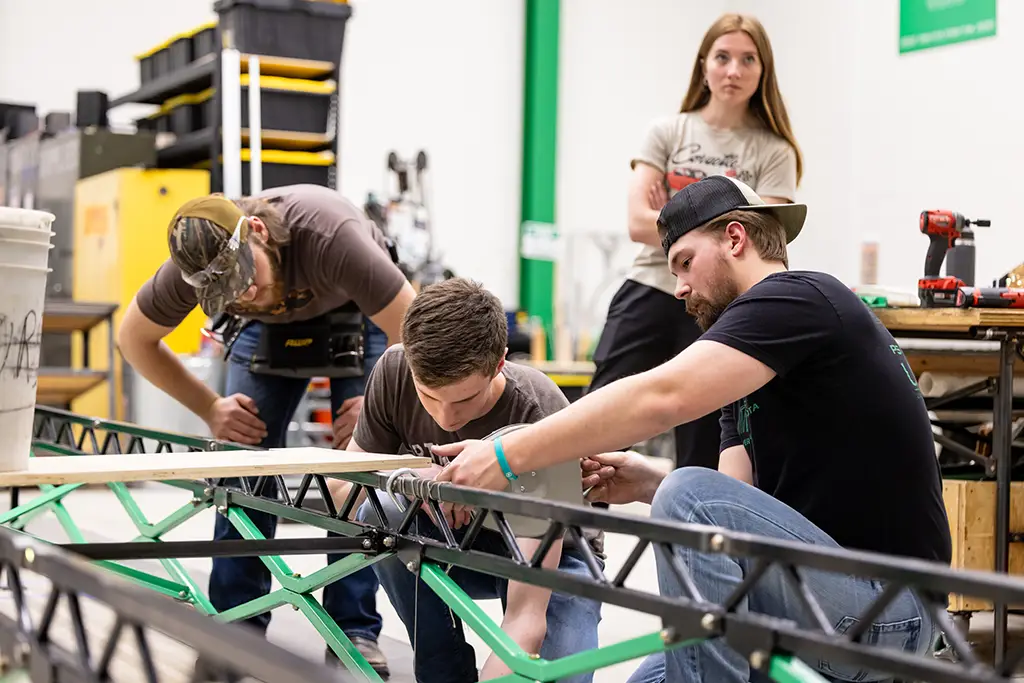 A team of civil engineering students collaborating on the design and structural testing of a large truss bridge project in the lab.