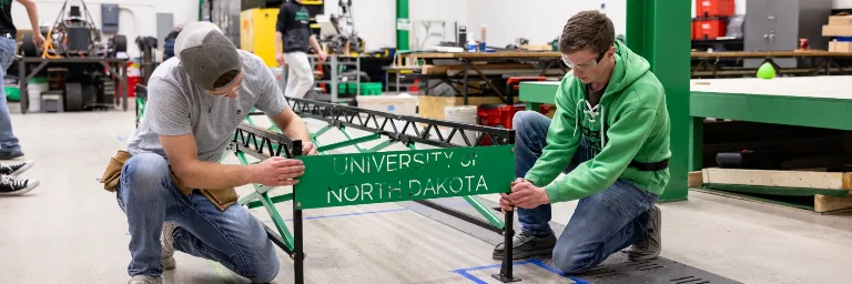 Two civil engineering students are working on a sign in a workshop.