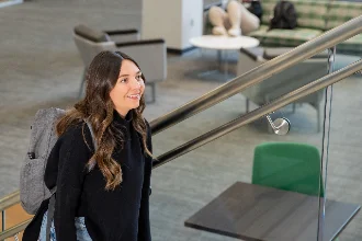 A business management student smiling while walking up a stairwell.