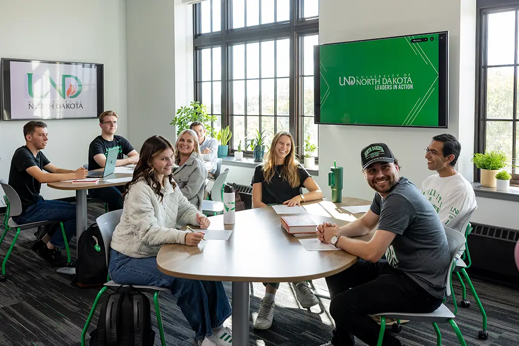Diverse students collaborating in a modern university classroom, discussing which Machine Learning or AI specialization they should focus on for their degree