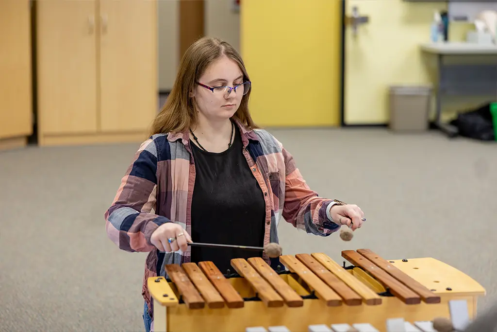A music therapy student plays a wooden xylophone with mallets in a clinical practice room.