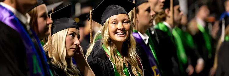Smiling engineering graduate celebrating at the university's commencement ceremony with peers.
