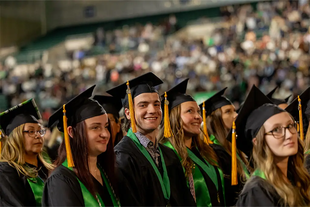 University graduates wearing caps and gowns smile during a commencement ceremony, celebrating the completion of their engineering degrees before continuing to graduate studies or professional specializations.