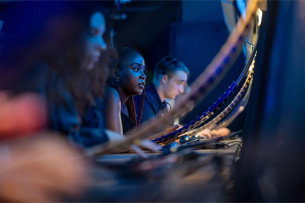 A row of air traffic control students wearing headsets monitor radar screens in a dimly lit lab.