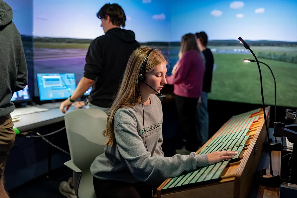 A student in a UND Aerospace sweatshirt and headset works a control panel in the tower simulator.
