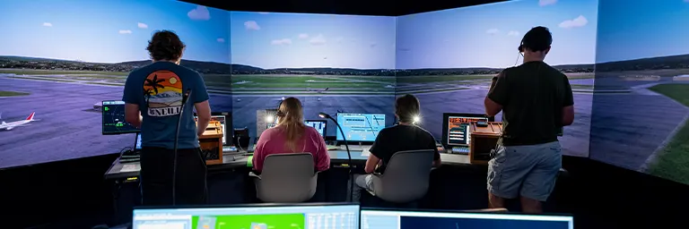 Four students staff air traffic control stations facing the curved runway screens of a tower simulator.