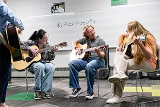 Three students play acoustic guitars together during a music class.