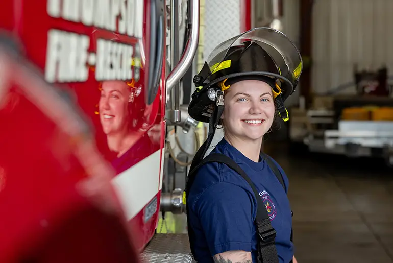 Ali Moses in firehat smiling next to a fire truck