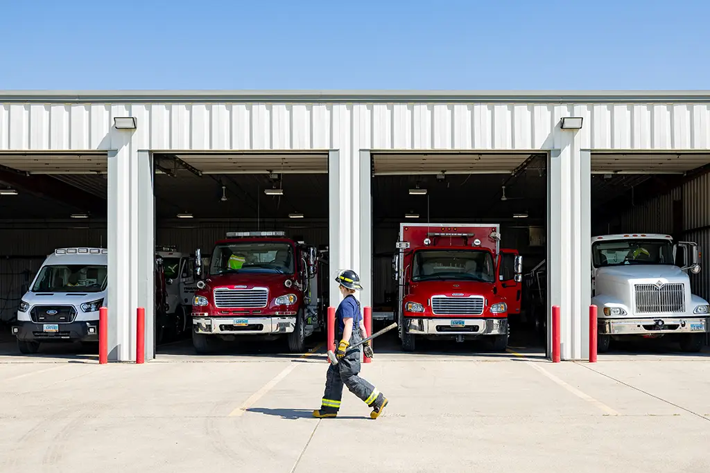 Ali walking in firefighter gear with fire trucks in background