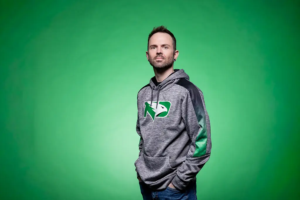 Austin standing in front of green screen in Fighting Hawks sweatshirt