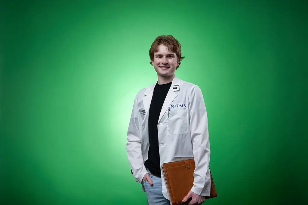 carson posing in front of green screen with UND diploma