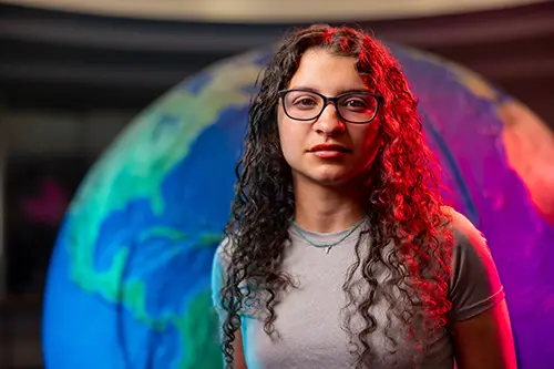 Kayla Barral standing in front of a large globe of Earth.