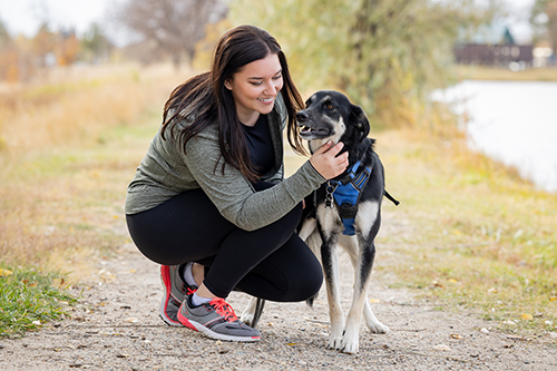 McKenzie Moe pets her dog while walking on a trail next to a lake