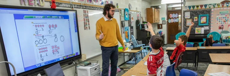 Elementary teacher in classroom teaching students math on smart screen