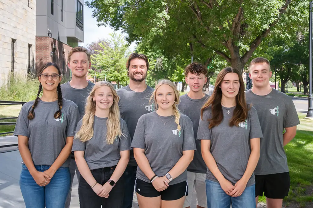 Group of young adults posing for photo with the sidewalk continuing on behind them