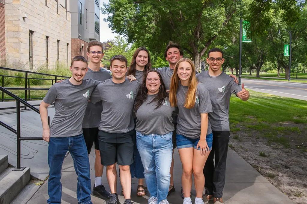 Group of young people pose for a photo with the side walk continuing behind them