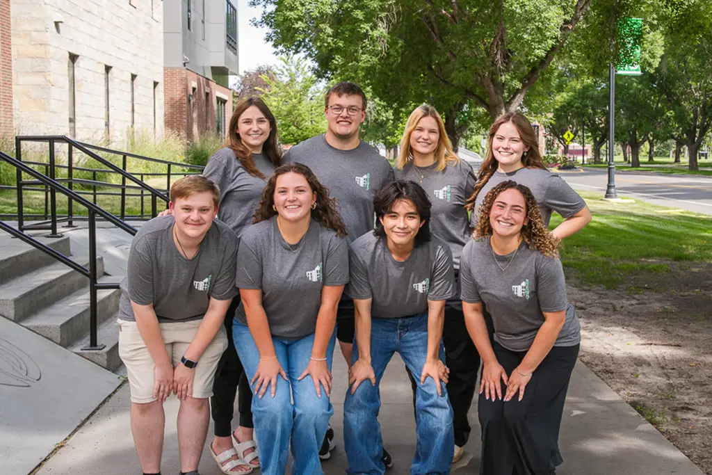 Group of young people pose for a photo with the side walk continuing behind them