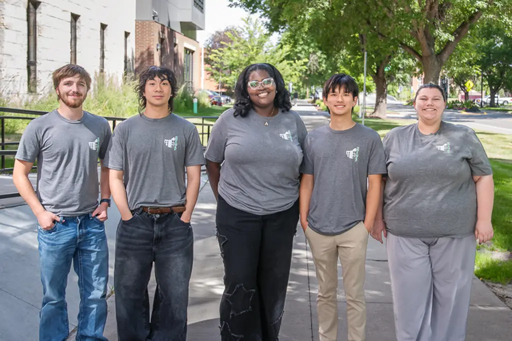 Group of young people pose for a photo with the side walk continuing behind them